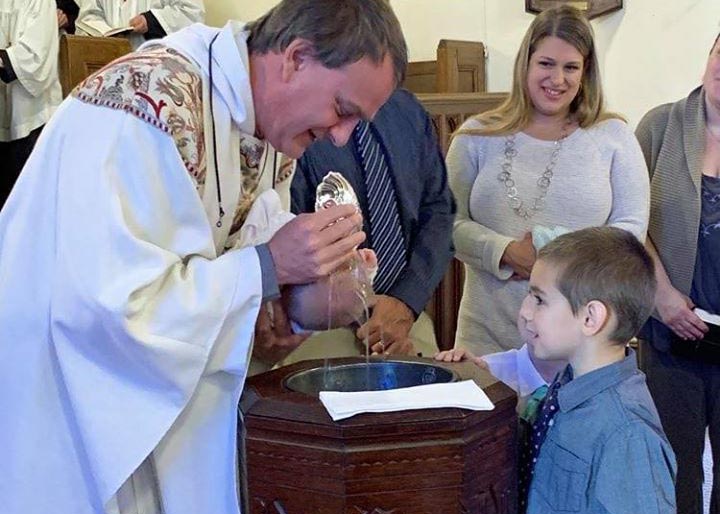 Reverend baptisizing a child at a service, proud parents look on